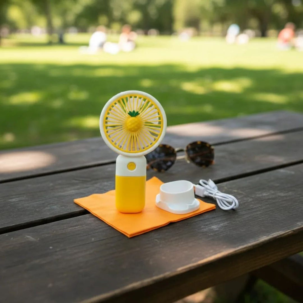 Yellow and white handheld fan on an orange cloth with sunglasses and a cable on a wooden table outdoors.